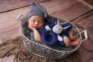 newborn baby sleeping in a basket with a gray hat and blue outfit